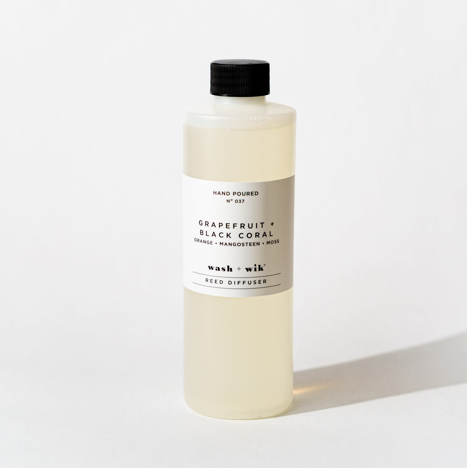 A bottle of Wash + Wik reed diffuser refill with a black cap and a minimalist white label, set against a clean white background with a soft shadow.