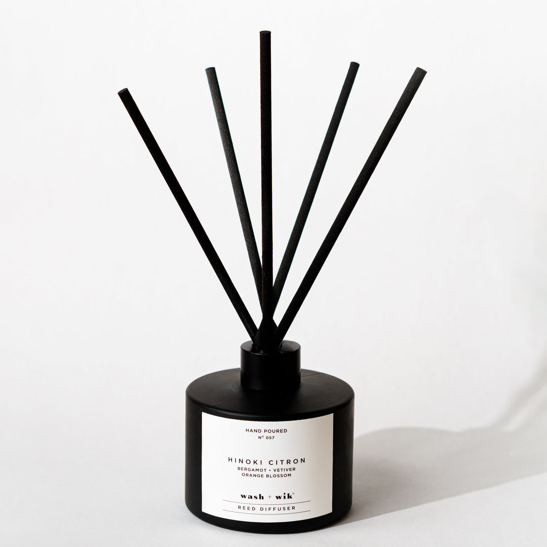 A black reed diffuser bottle with a black cap and five black reeds