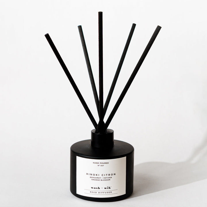 A black reed diffuser bottle with a black cap and five black reeds