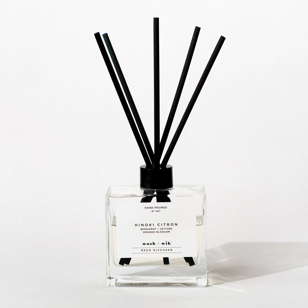A clear glass reed diffuser bottle with a black cap and five black reeds