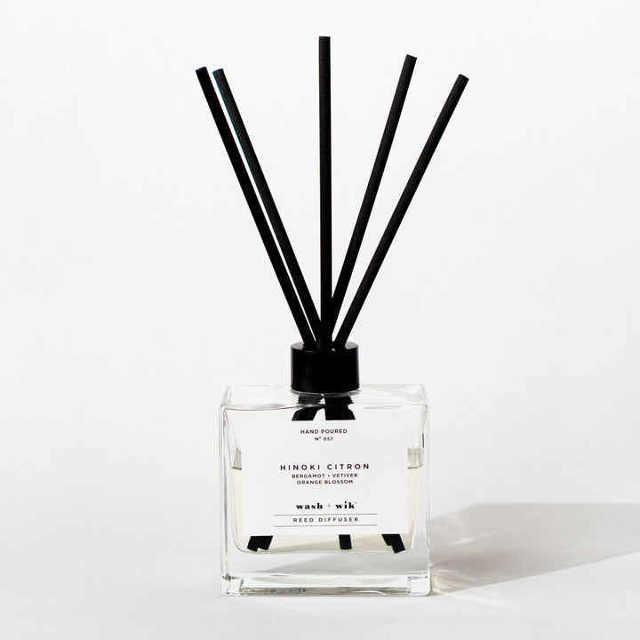 A clear glass reed diffuser bottle with a black cap and five black reeds
