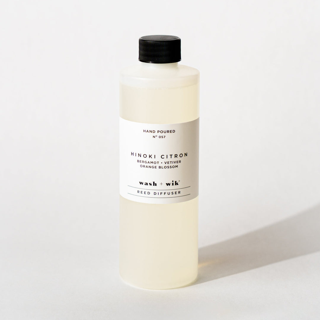 A bottle of Wash + Wik reed diffuser refill with a black cap and a minimalist white label, set against a clean white background with a soft shadow.