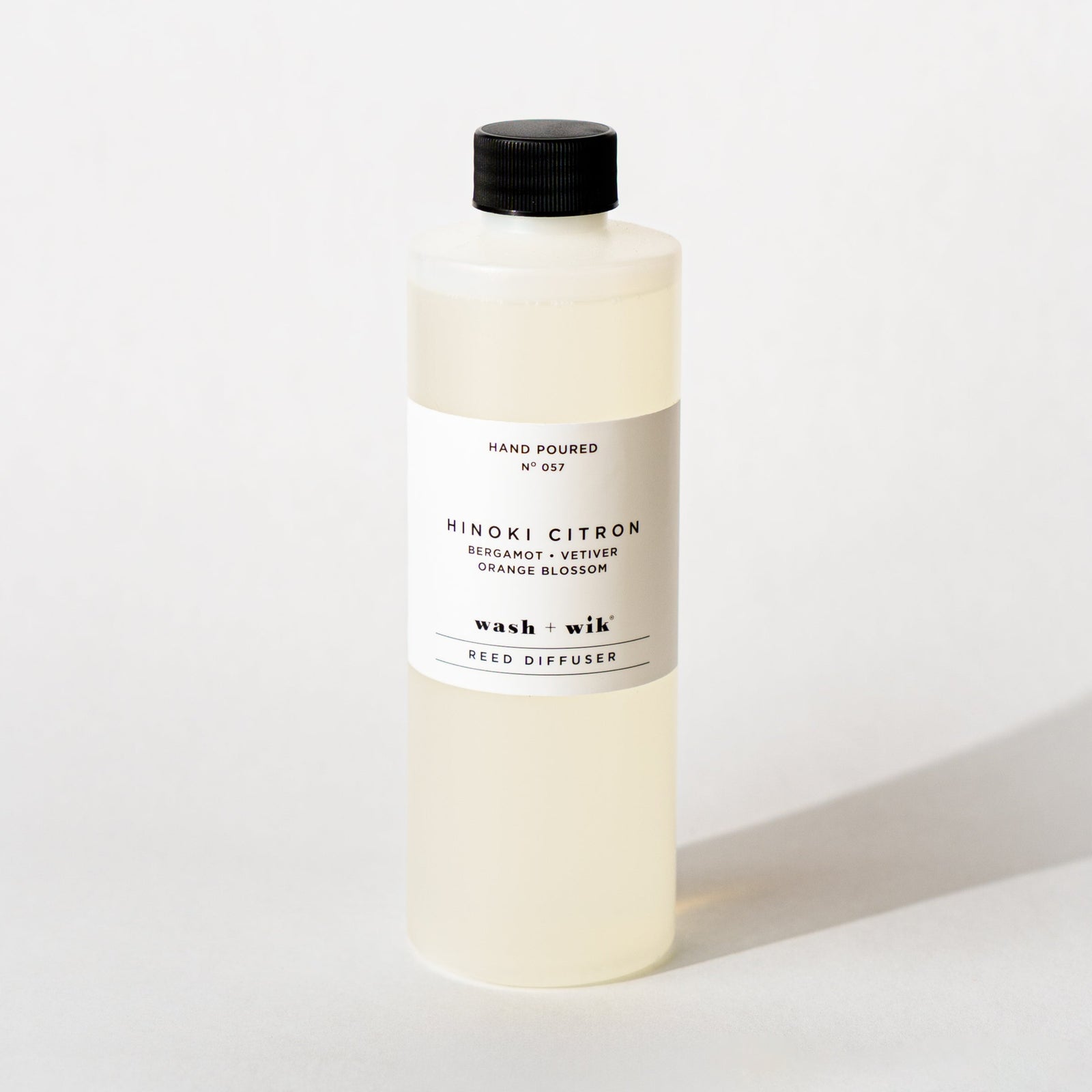 A bottle of Wash + Wik reed diffuser refill with a black cap and a minimalist white label, set against a clean white background with a soft shadow.