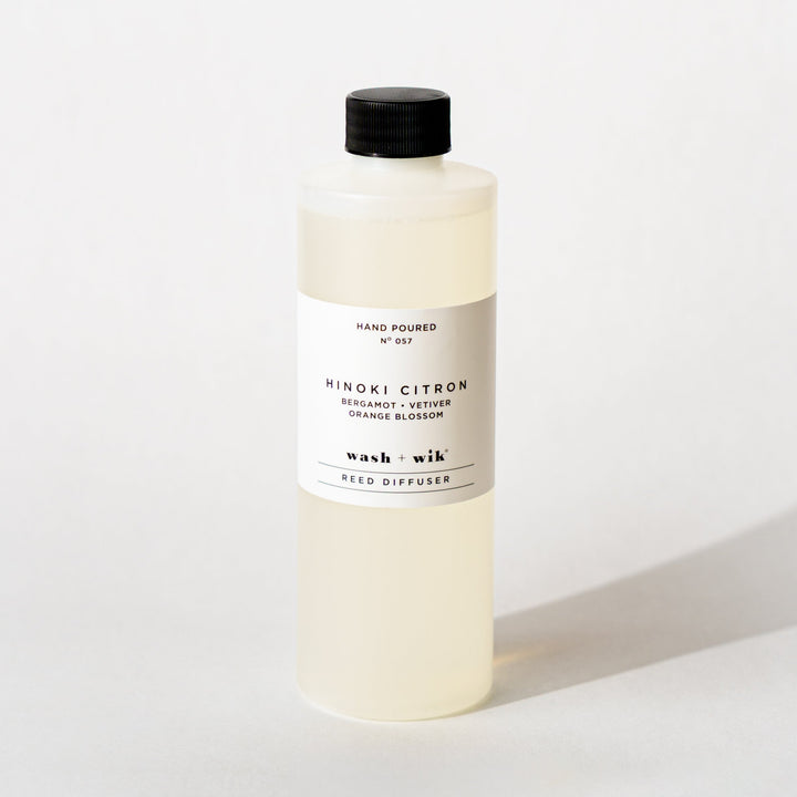 A bottle of Wash + Wik reed diffuser refill with a black cap and a minimalist white label, set against a clean white background with a soft shadow.