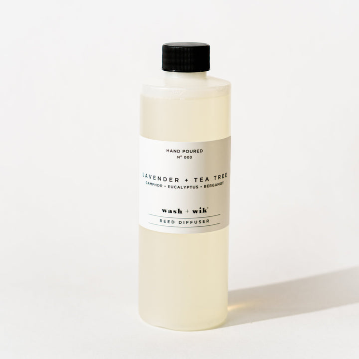 A bottle of Wash + Wik reed diffuser refill with a black cap and a minimalist white label, set against a clean white background with a soft shadow.