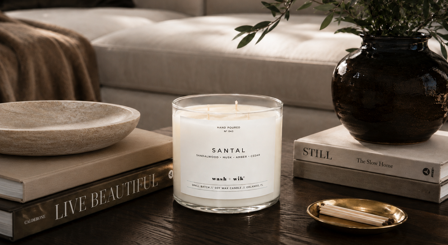 Candle labeled 'Santal' on a table with books and decorative items.