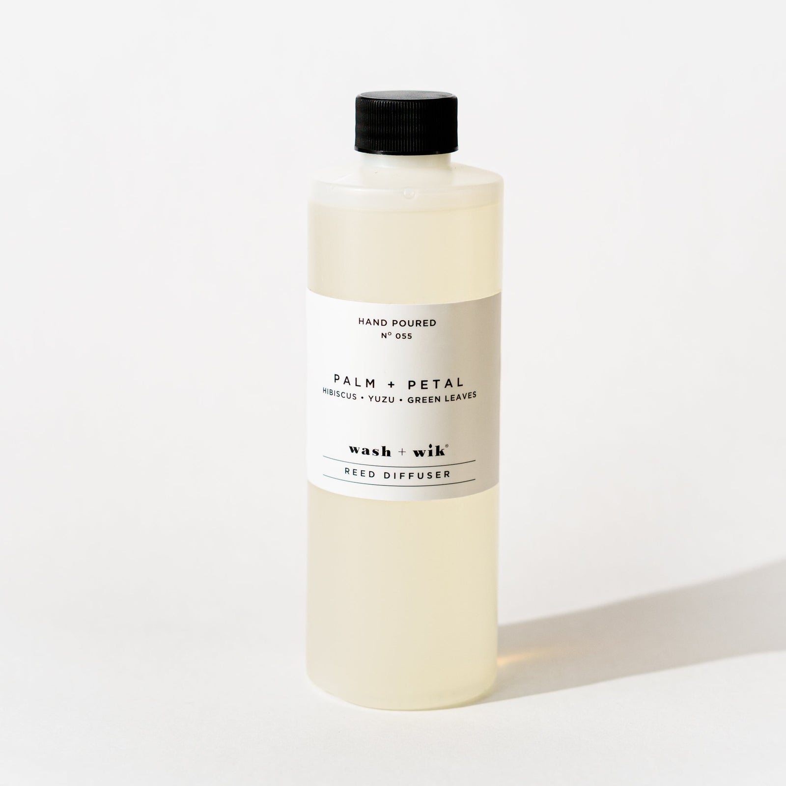 A bottle of Wash + Wik reed diffuser refill with a black cap and a minimalist white label, set against a clean white background with a soft shadow.