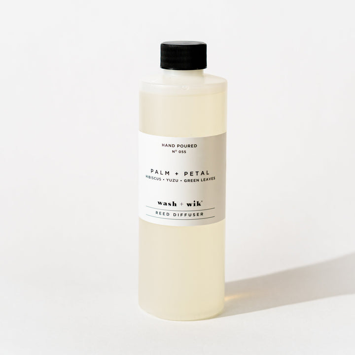 A bottle of Wash + Wik reed diffuser refill with a black cap and a minimalist white label, set against a clean white background with a soft shadow.
