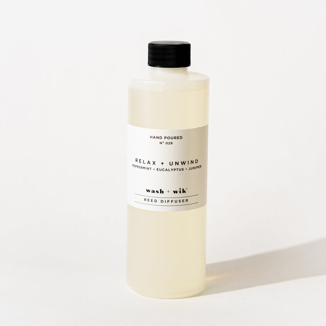 A bottle of Wash + Wik reed diffuser refill with a black cap and a minimalist white label, set against a clean white background with a soft shadow.