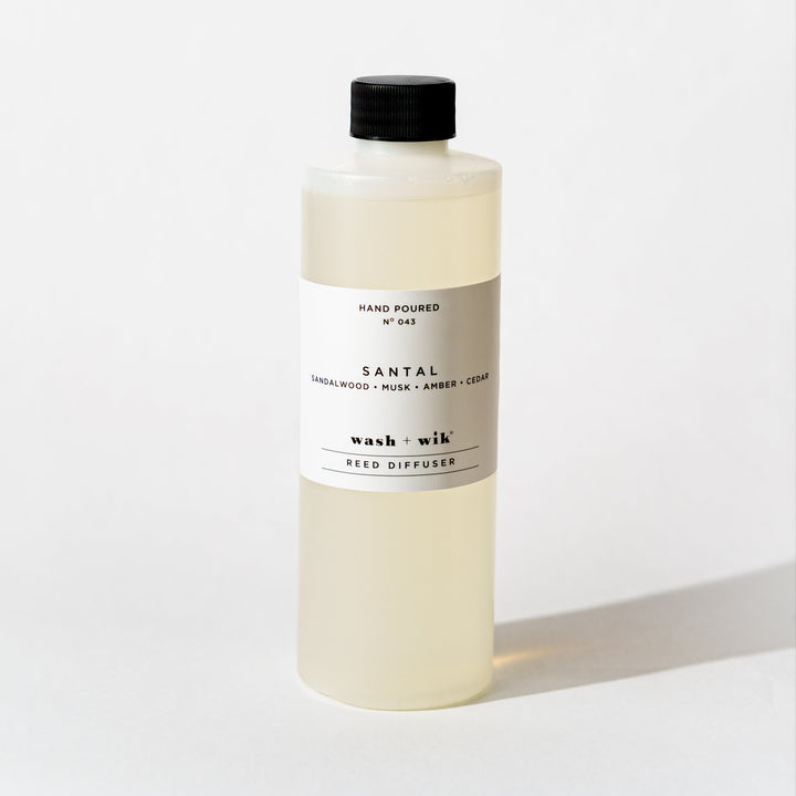 A bottle of Wash + Wik reed diffuser refill with a black cap and a minimalist white label, set against a clean white background with a soft shadow.