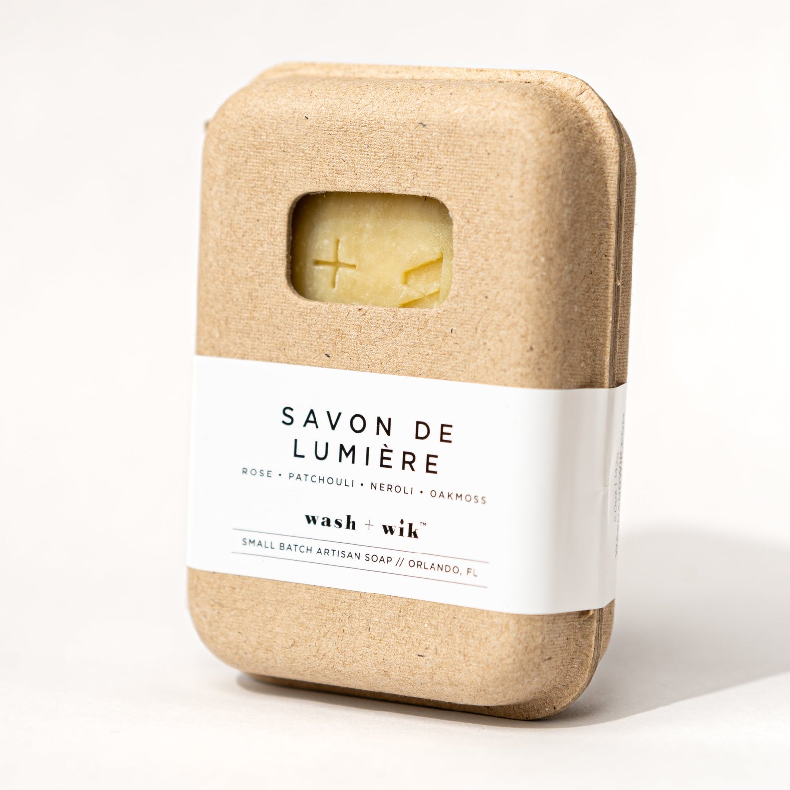 Bar of soap in a brown paper wrap with 'Savon de Lumiere' branding on a white background