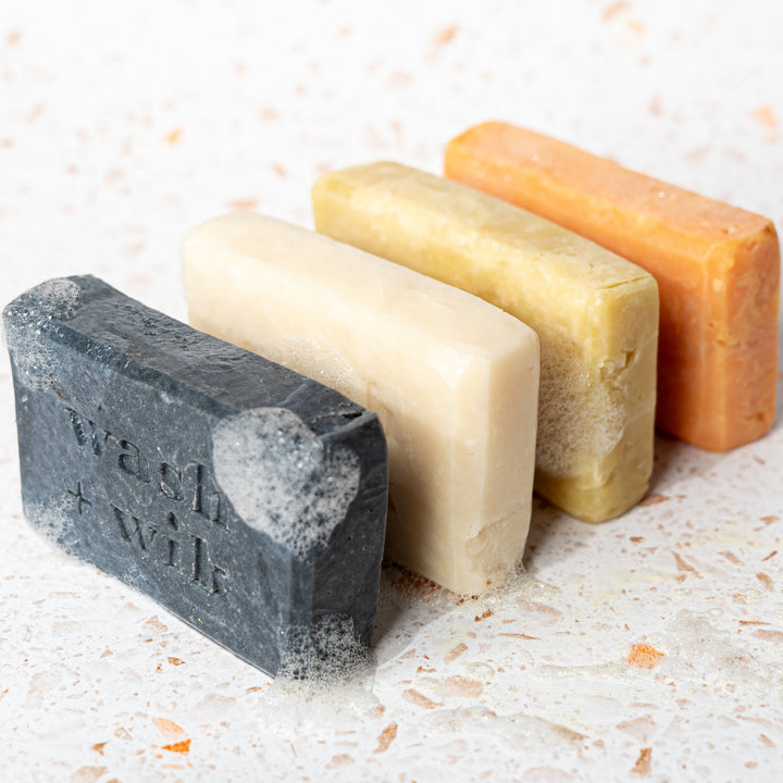 Four bars of soap in different colors on a textured surface