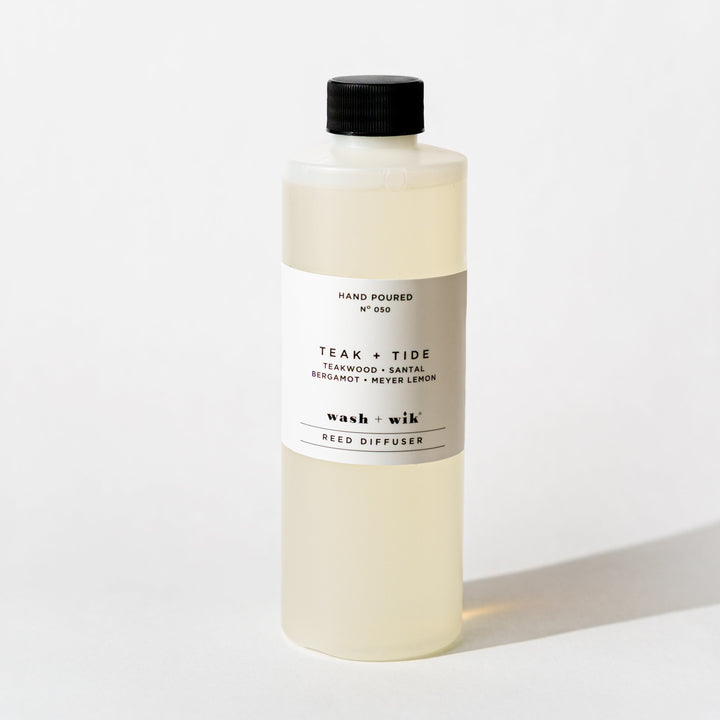 A bottle of Wash + Wik reed diffuser refill with a black cap and a minimalist white label, set against a clean white background with a soft shadow.
