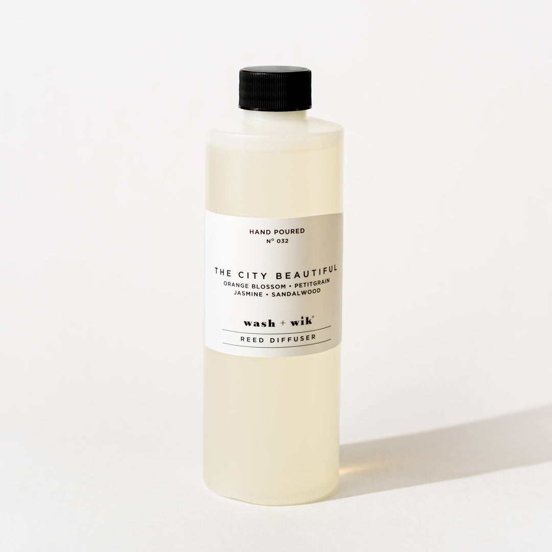 A bottle of Wash + Wik reed diffuser refill with a black cap and a minimalist white label, set against a clean white background with a soft shadow.