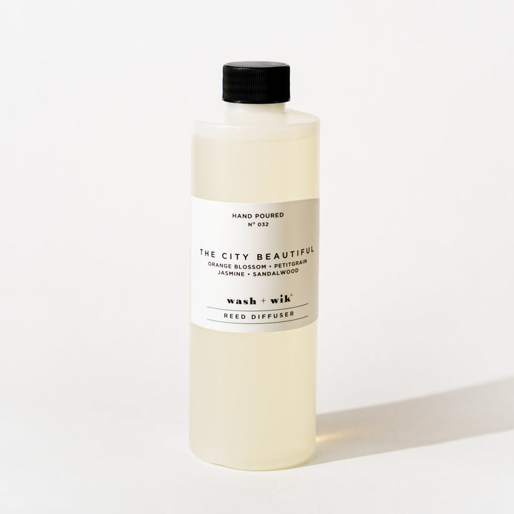 A bottle of Wash + Wik reed diffuser refill with a black cap and a minimalist white label, set against a clean white background with a soft shadow.