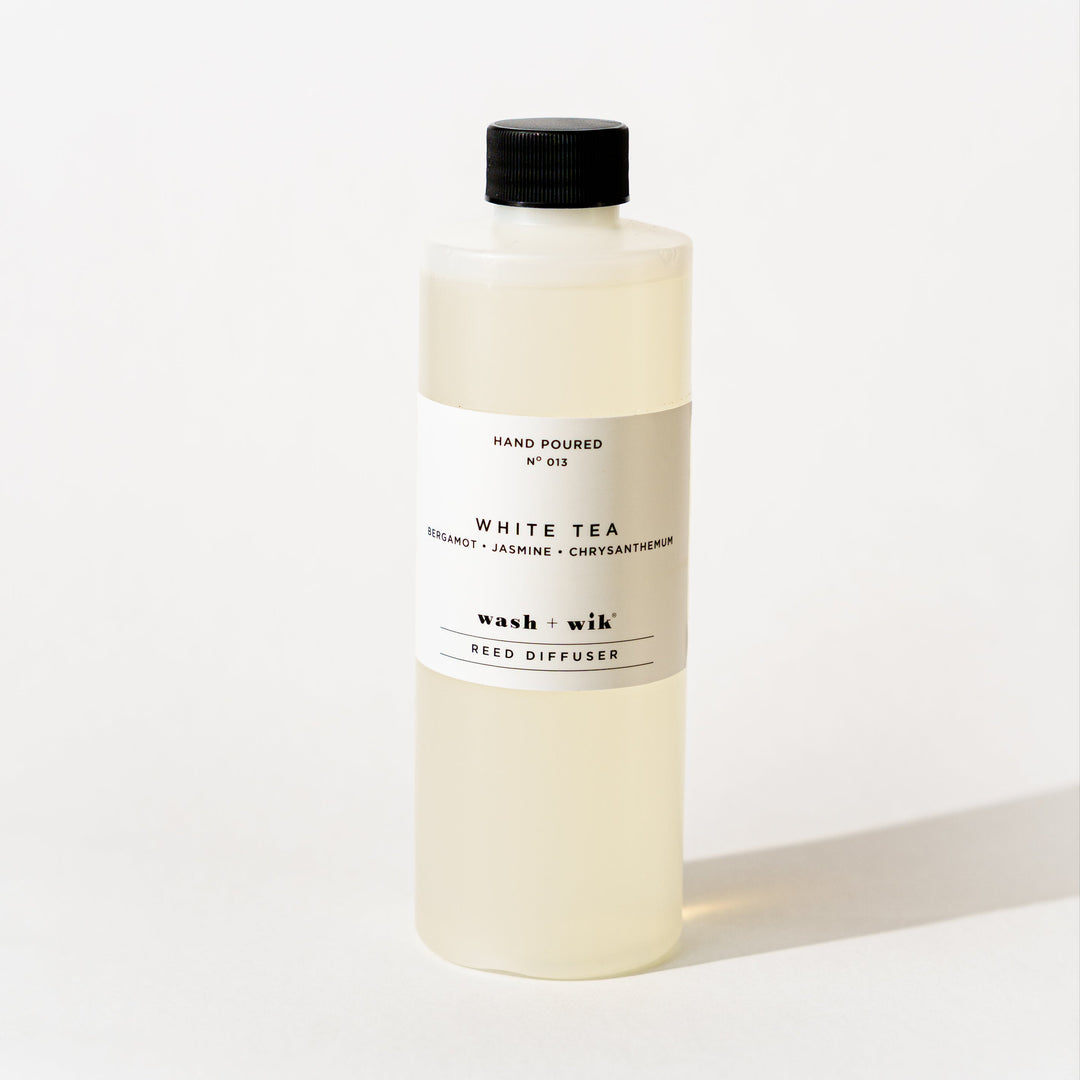 A bottle of Wash + Wik reed diffuser refill with a black cap and a minimalist white label, set against a clean white background with a soft shadow.