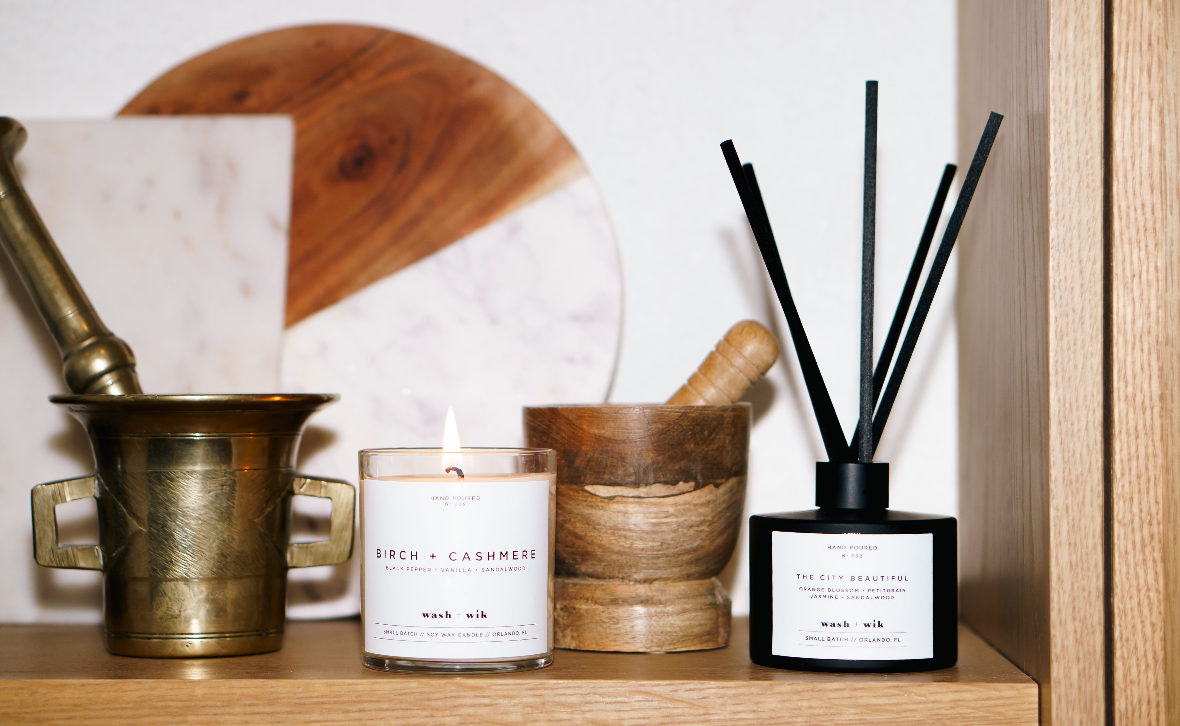 Lifestyle image that shows a candle and a reed diffuser on a shelf with other household products 