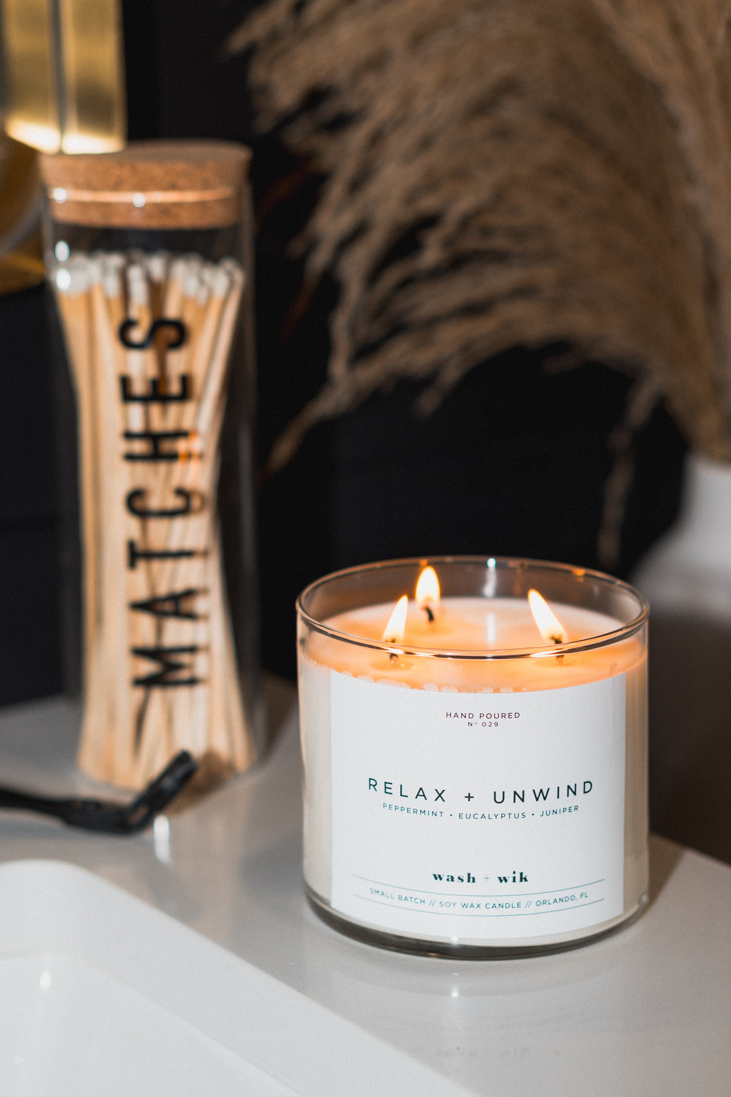 Candle labeled 'Relax & Unwind' next to a matches container on a surface.