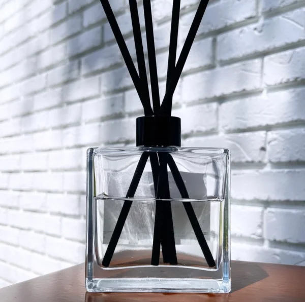 A square glass container with black sticks in it.