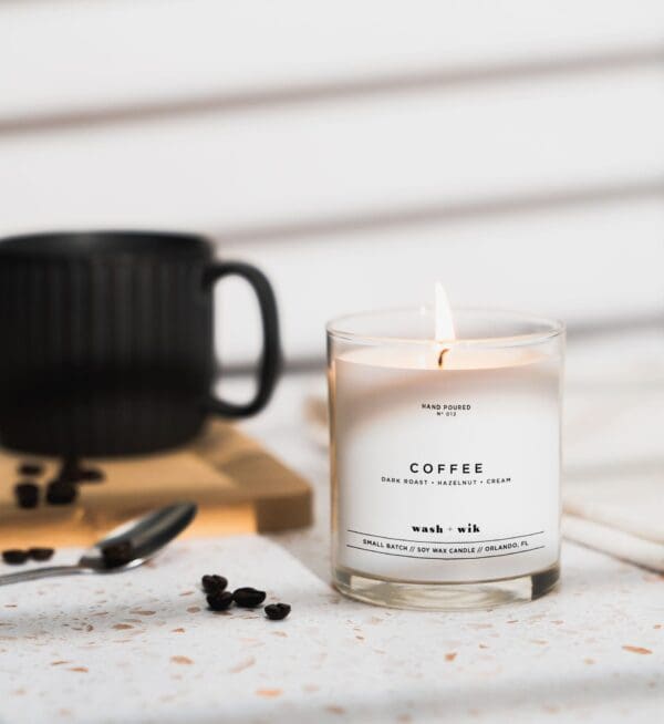 A candle sitting on top of a table next to a cup.