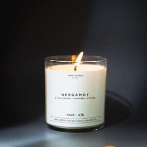 A candle lit in a glass container with the label " bergamot ".