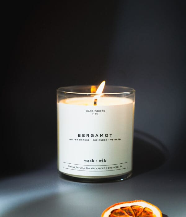 A candle lit in a glass container with the label " bergamot ".